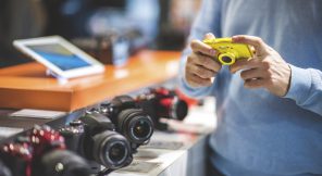 Unrecognizable male customer is holding yellow camera in the store. Row of other camera models is visible on the shelf.